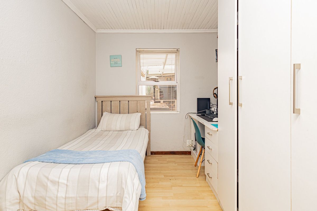 A compact bedroom featuring laminate flooring, a timber ceiling, and a built-in wardrobe, offering a functional space with natural light.