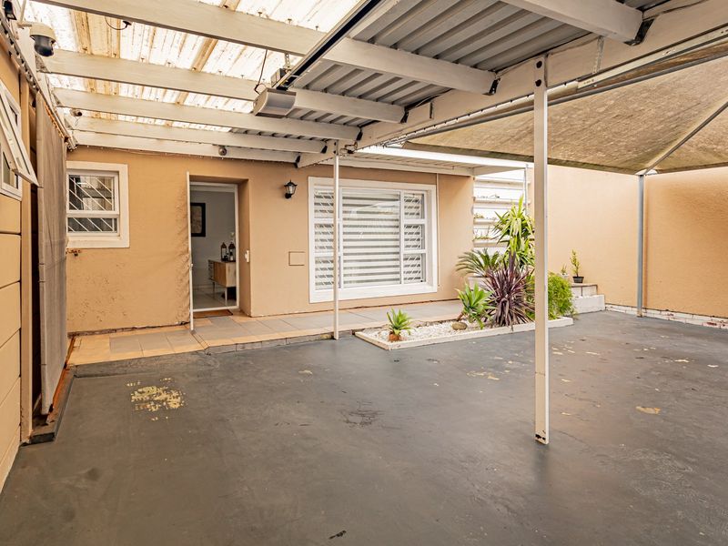 A covered outdoor patio area featuring paved flooring, translucent roofing, and security bars on windows, providing a functional space for outdoor living.