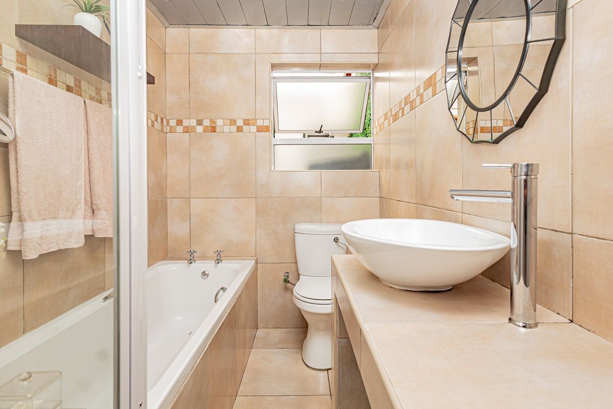 A compact bathroom featuring a built-in bathtub, a modern vessel sink with chrome faucet, and neutral wall tiling throughout.
