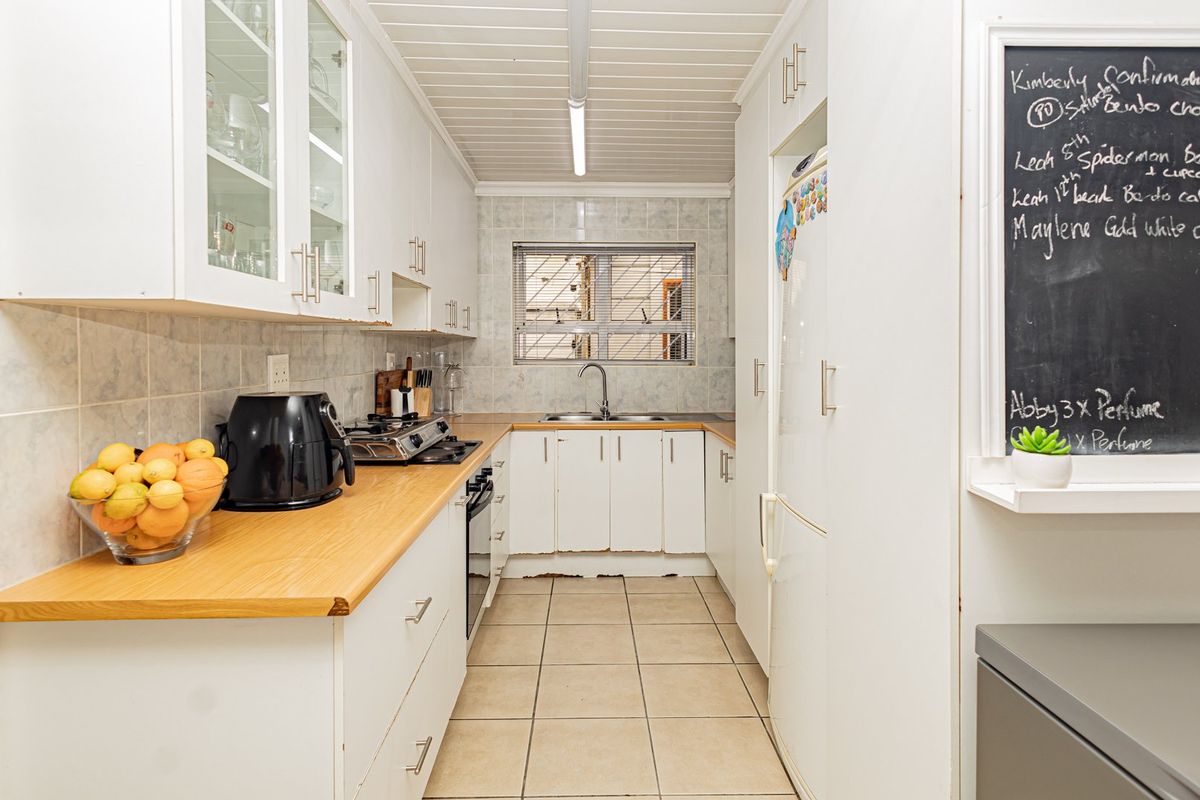 A functional galley-style kitchen featuring white cabinetry, laminate countertops, a gas hob, built-in oven, and tiled flooring with a neutral backsplash.
