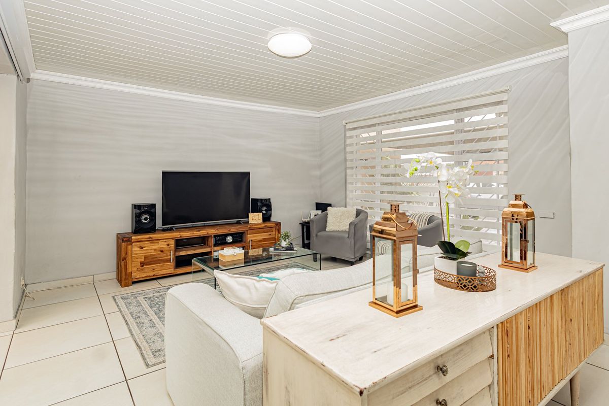 A bright living room featuring tiled flooring, a tongue and groove ceiling, and roller blinds, offering a comfortable and functional living space.