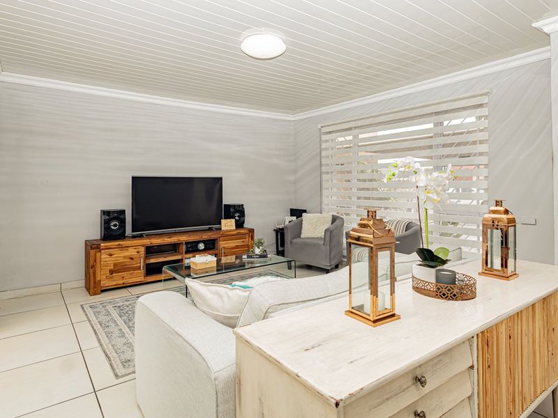 A bright living room featuring tiled flooring, a tongue and groove ceiling, and roller blinds, offering a comfortable and functional living space.