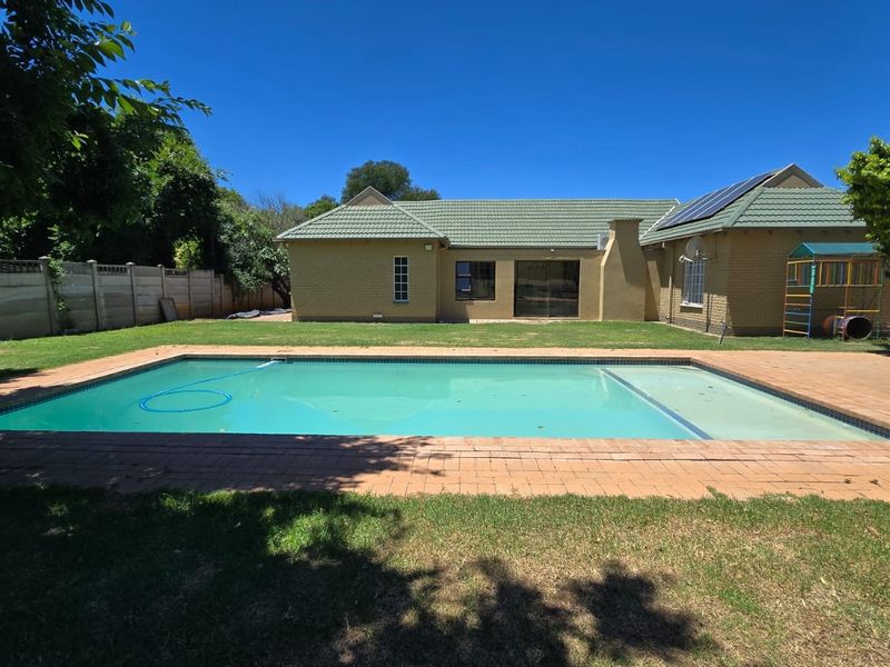 Rear view of the property featuring a swimming pool, brick paved surround, and a well-maintained garden area with solar panels on the roof.