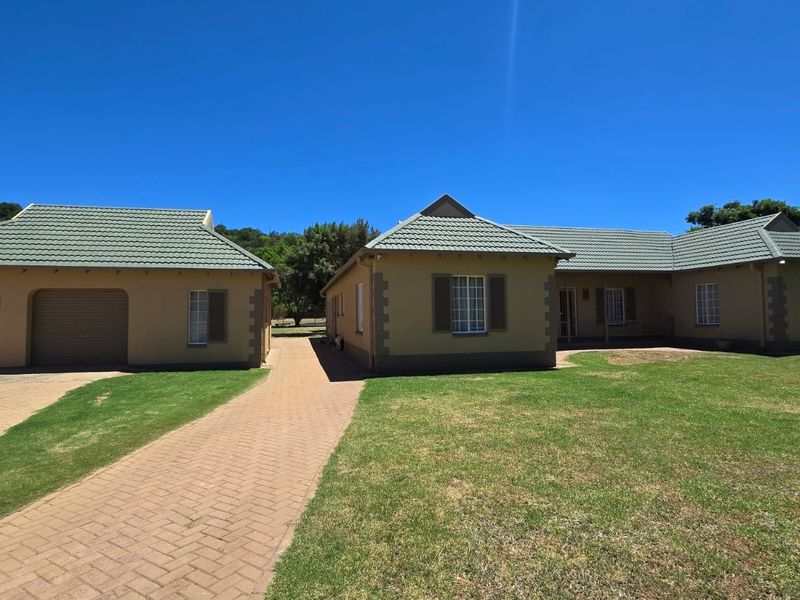 Front view of a well-maintained farm property featuring a double garage, paved driveway, and landscaped lawn under a clear blue sky.