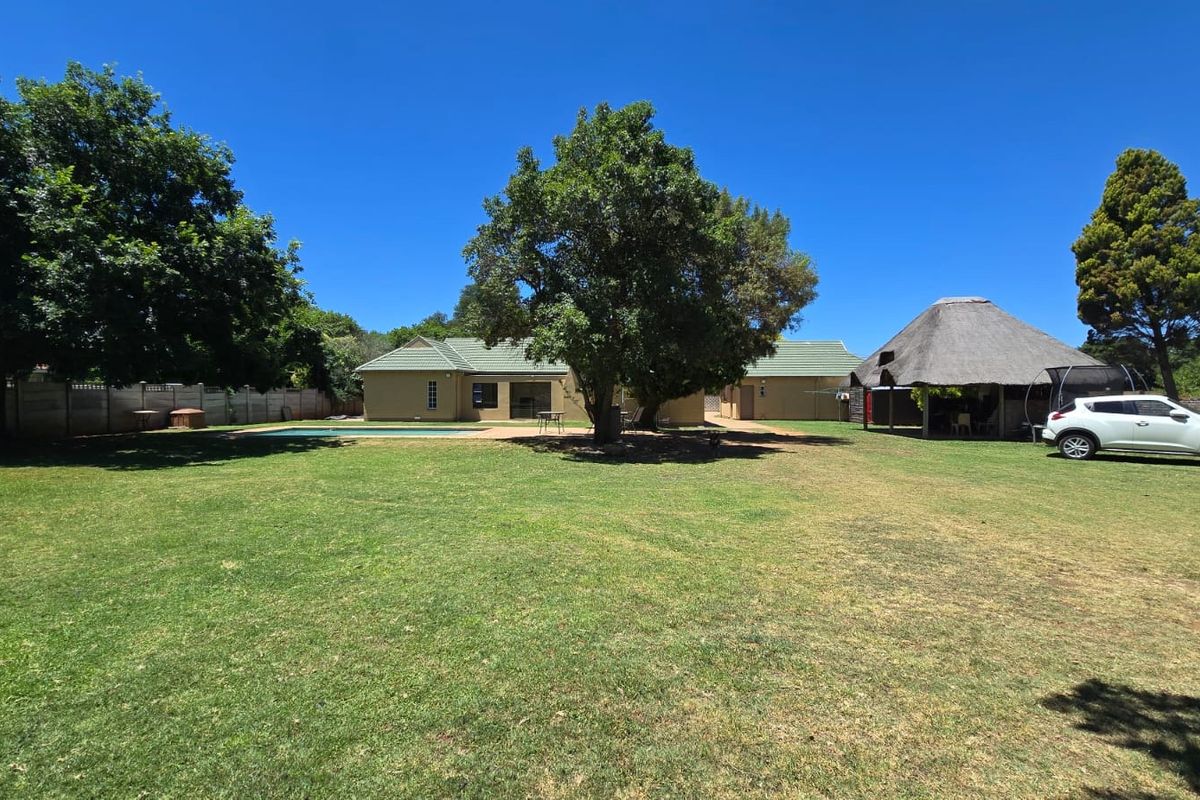 Spacious rear garden featuring a swimming pool, a traditional thatched lapa, and established trees, providing a private outdoor entertainment area.