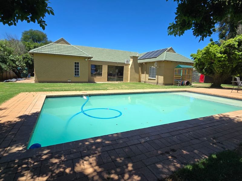 A well-maintained rear garden featuring a swimming pool with brick paving, solar panels on the tiled roof, and clear access to the main dwelling.