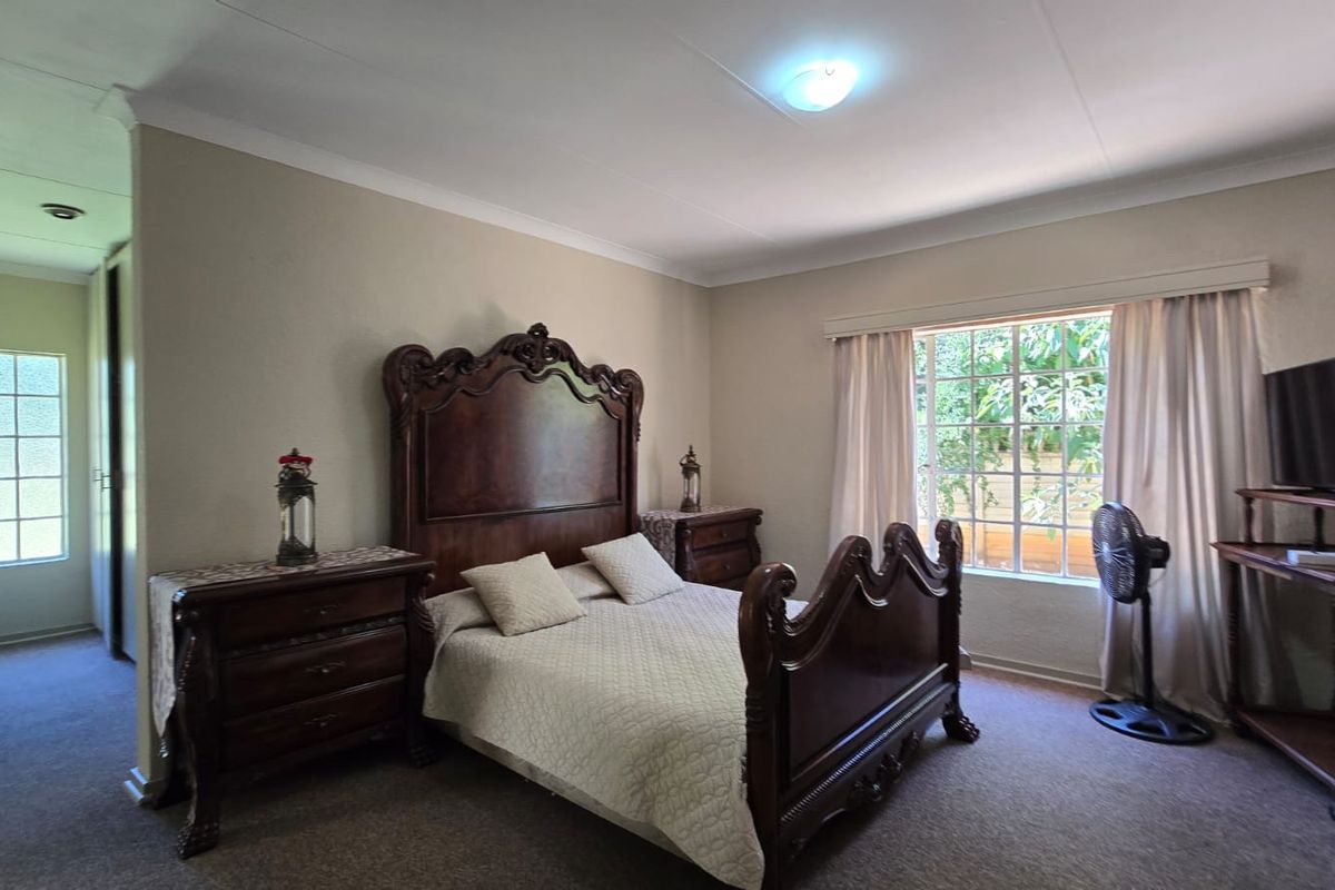 A spacious bedroom featuring neutral walls, carpeted flooring, built-in cupboards, and a window with security bars allowing natural light.