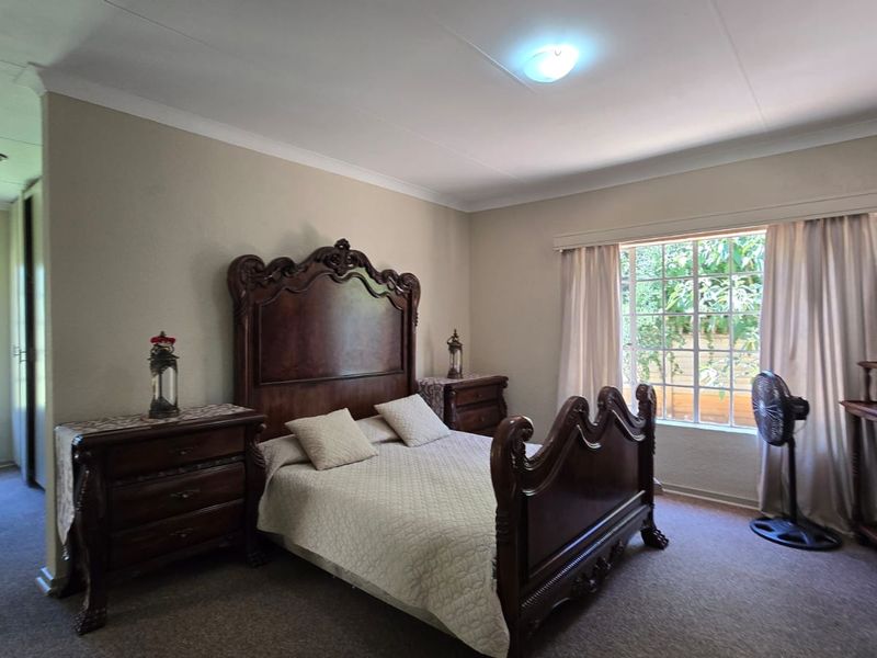 A spacious bedroom featuring neutral walls, carpeted flooring, built-in cupboards, and a window with security bars allowing natural light.