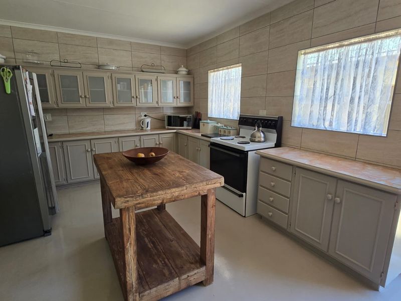 A functional kitchen featuring neutral-toned built-in cabinetry, laminate countertops, a tiled splashback, and a freestanding stove, offering a practical layout for daily meal preparation.