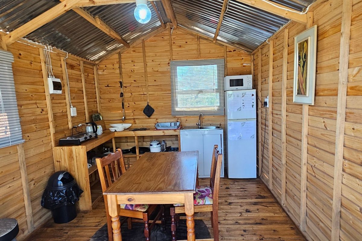 A rustic timber-clad kitchen area featuring exposed corrugated metal roofing, wooden flooring, and basic sink installation within a compact cabin-style structure.