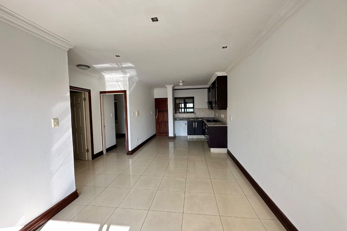 An open-plan living and kitchen area featuring neutral tiled flooring, dark cabinetry with granite countertops, and recessed lighting throughout the space.