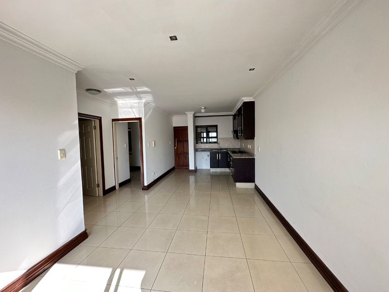 An open-plan living and kitchen area featuring neutral tiled flooring, dark cabinetry with granite countertops, and recessed lighting throughout the space.