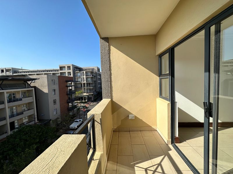 A clean, tiled balcony featuring a metal balustrade and sliding glass door access, offering an elevated view of the surrounding urban apartment complex.