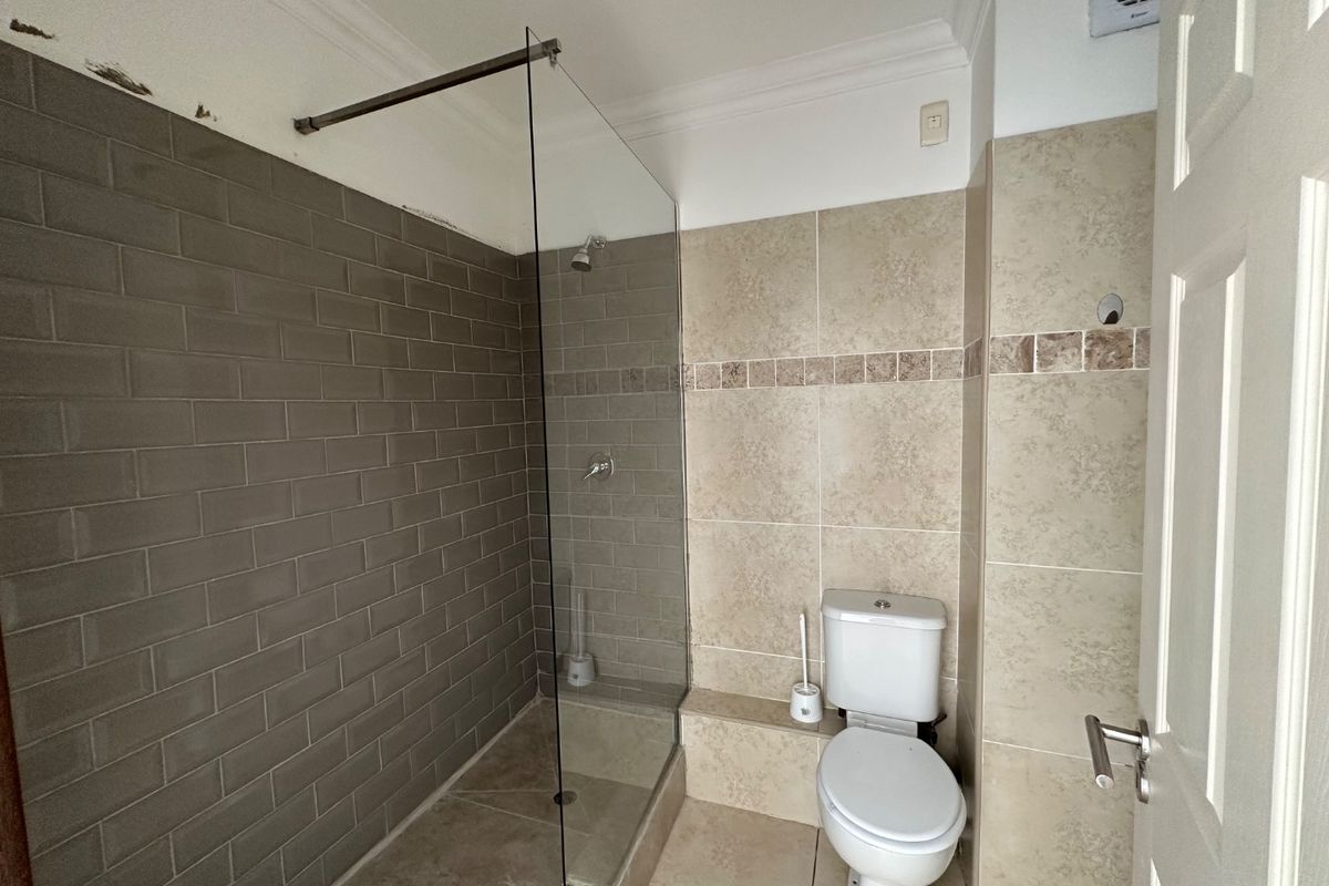 A functional bathroom featuring a walk-in shower with a glass screen, tiled walls, and a standard toilet, requiring minor finishing touches to the paintwork.
