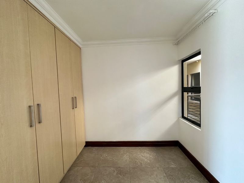 An empty bedroom featuring light wood-finish built-in cupboards, tiled flooring, and a window with an aluminium frame.