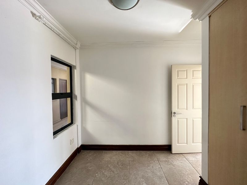 An empty bedroom featuring tiled flooring, built-in cupboards, and neutral wall finishes, offering a clean and versatile space ready for personalization.