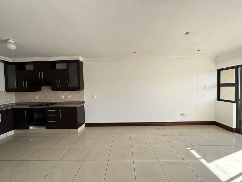 Spacious open-plan living area featuring a modern kitchen with dark cabinetry, granite countertops, built-in appliances, and neutral tiled flooring throughout.