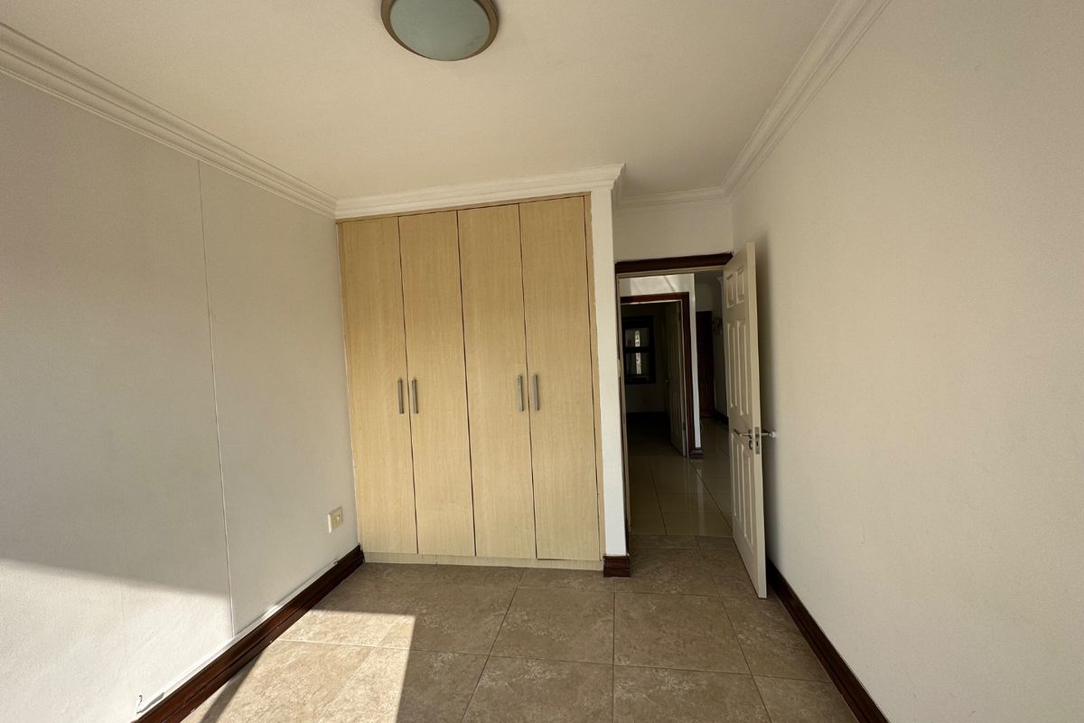 A clean, empty bedroom featuring neutral tiled flooring, built-in wooden cupboards, and classic ceiling coving, offering a versatile space ready for personalization.