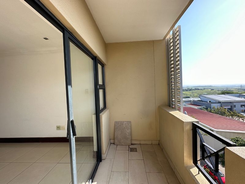 A covered balcony featuring tiled flooring, a metal balustrade, and a louvered privacy screen, offering an open view of the surrounding area.