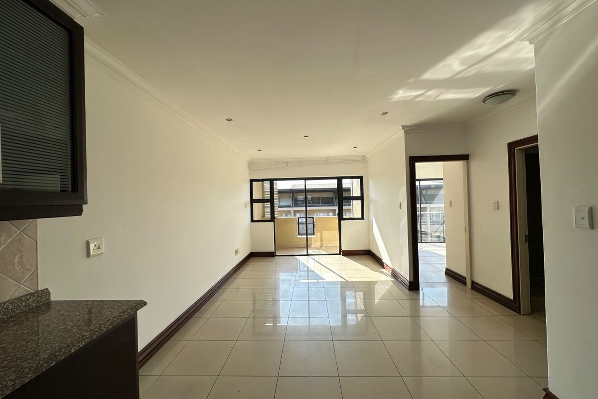 Spacious open-plan living area featuring neutral tiled flooring, recessed lighting, and direct access to a balcony through sliding glass doors.