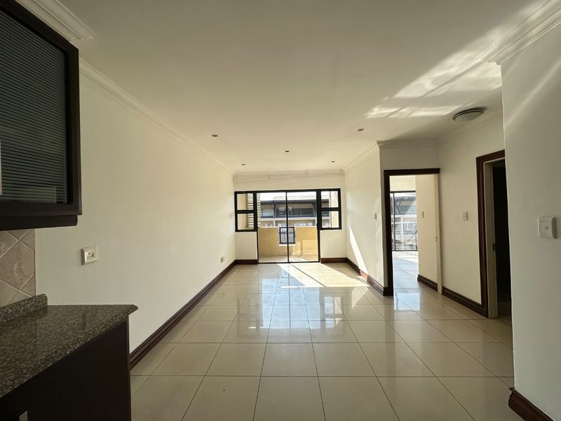 Spacious open-plan living area featuring neutral tiled flooring, recessed lighting, and direct access to a balcony through sliding glass doors.