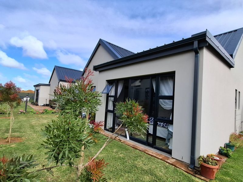 A well-maintained rear exterior view of a modern house featuring a metal roof, stone cladding accents, and large sliding glass doors opening to the garden.