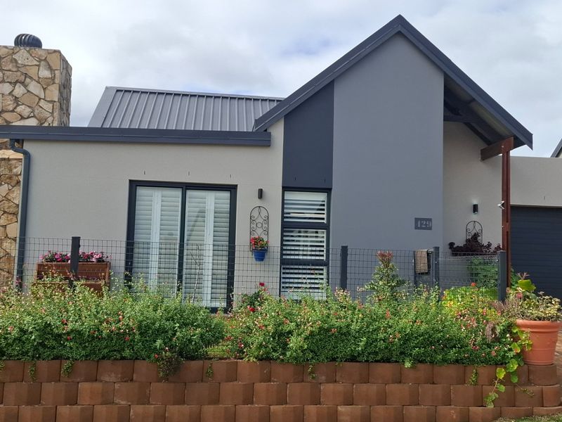 Modern single-story home featuring a stone-clad chimney, metal roof, and a paved driveway with a well-maintained front garden and retaining wall.
