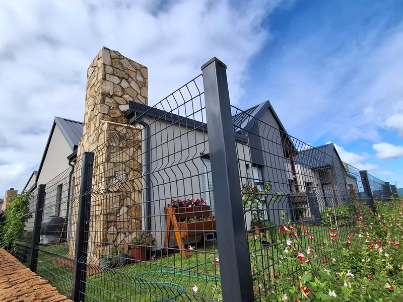 Rear view of a modern house featuring a prominent stone chimney, metal roofing, and secure wire mesh perimeter fencing.