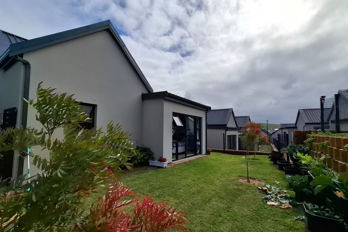 Rear view of a modern house featuring a well-maintained lawn, sliding glass doors, and a tiered retaining wall garden area.