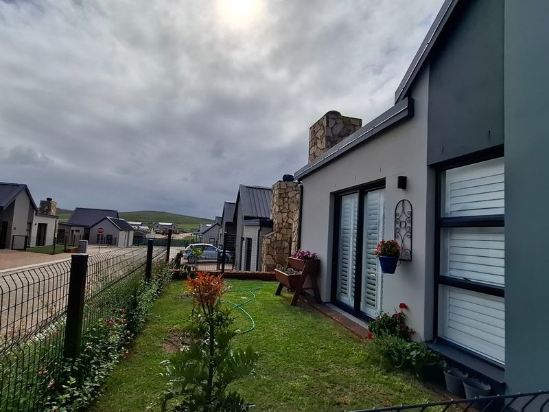 A view of the rear exterior of the house featuring a stone-clad chimney, sliding glass doors, and a well-maintained garden area.