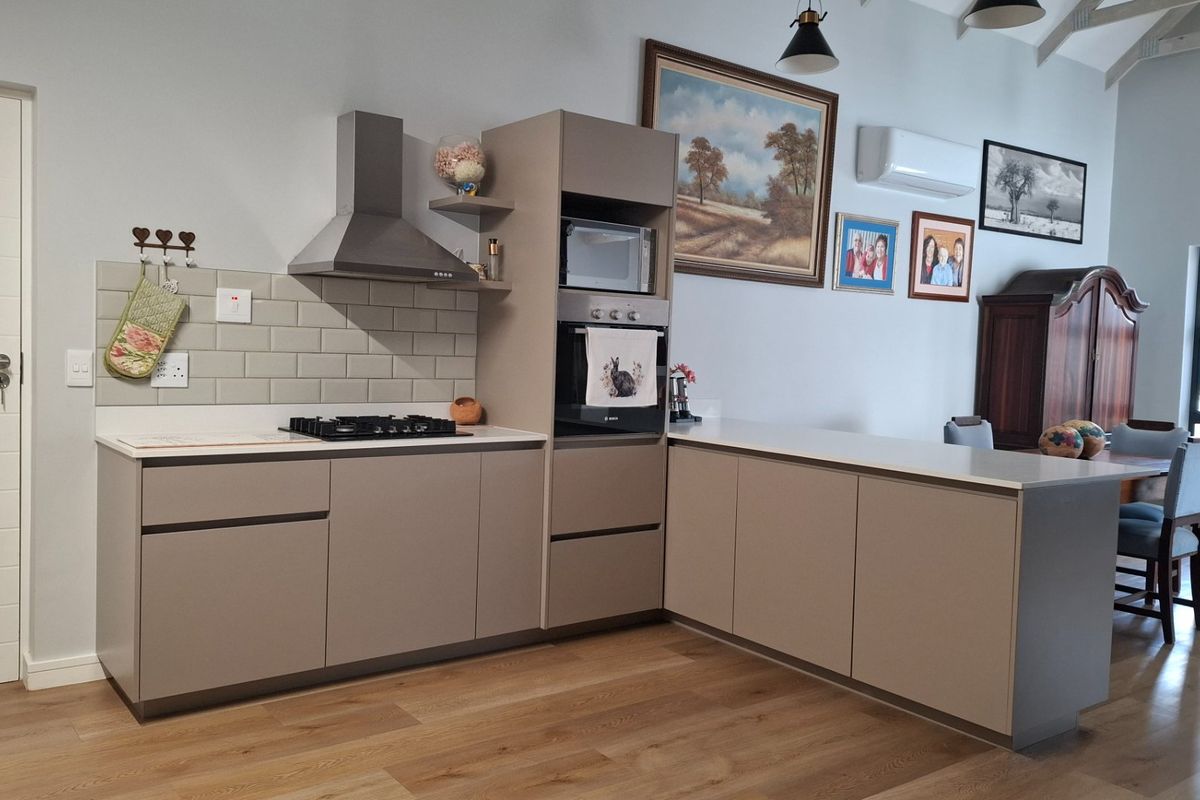 Modern kitchen featuring sleek cabinetry, built-in appliances, subway tile backsplash, and laminate flooring, set within an open-plan living space with vaulted ceilings.
