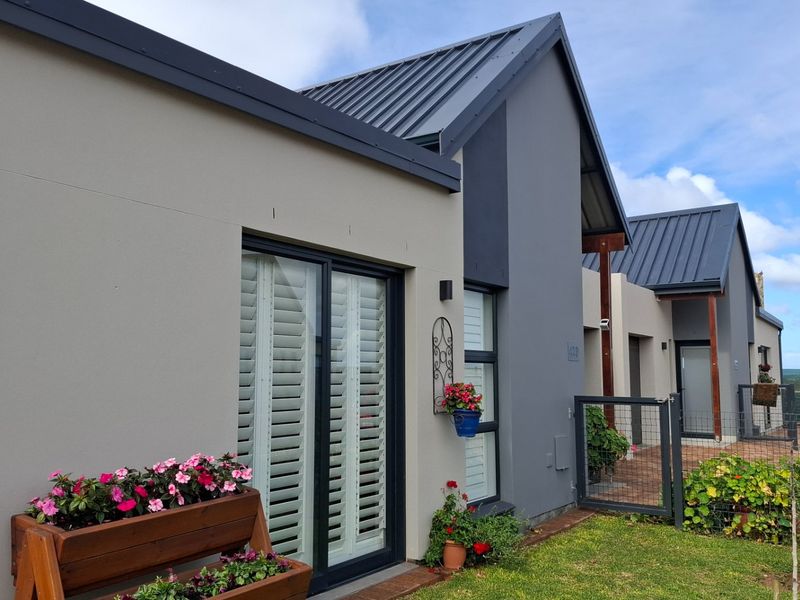 A modern rear exterior view of the house featuring a contemporary metal roof, sliding glass doors with shutters, and a well-maintained garden area.