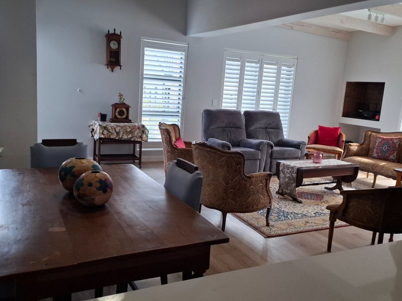 Spacious open-plan living and dining area featuring light laminate flooring, exposed ceiling beams, plantation shutters, and a built-in recessed fireplace.