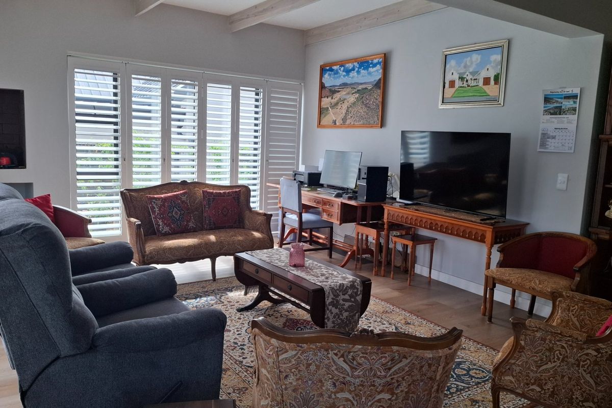 A spacious living room featuring hardwood flooring, exposed ceiling beams, and plantation shutters, creating a bright and comfortable atmosphere.