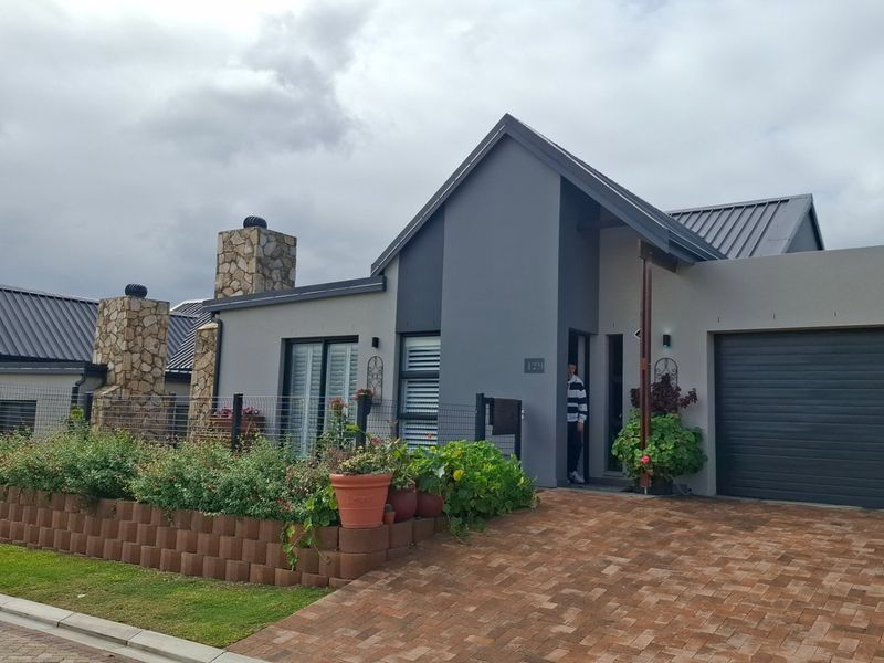 Modern single-story residence featuring a stone-clad chimney, metal roofing, and a paved driveway with a well-maintained front garden.