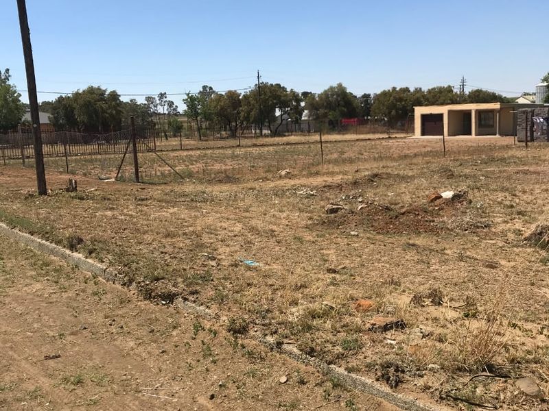 A vacant residential plot featuring perimeter fencing, concrete curbing, and a utility pole, offering a clear space for potential development.