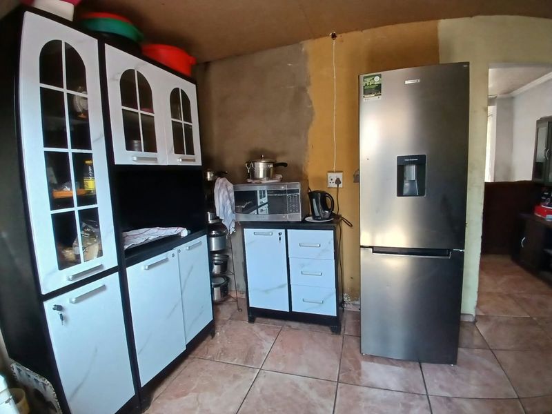 A kitchen area featuring tiled flooring and built-in cabinetry, currently requiring wall finishing and electrical maintenance to improve the overall aesthetic and functionality.