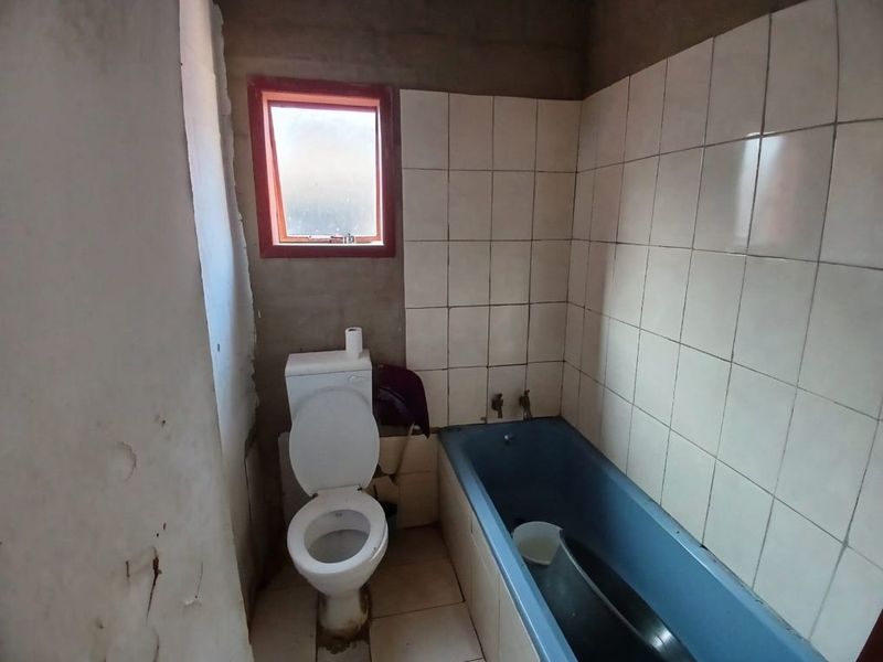 A small bathroom featuring a bathtub and toilet, currently in need of significant renovation and finishing of wall surfaces.