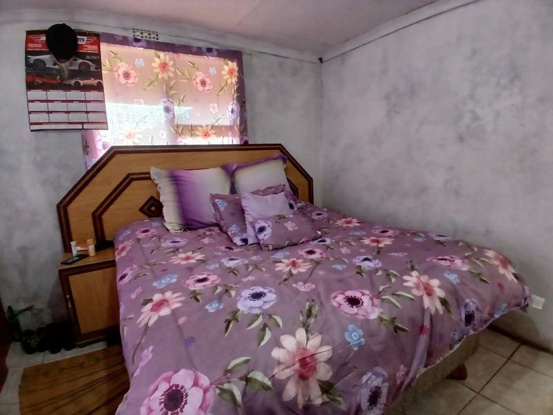 A bedroom featuring tiled flooring and a built-in headboard, requiring cosmetic updates to the wall finishes to improve the overall aesthetic.