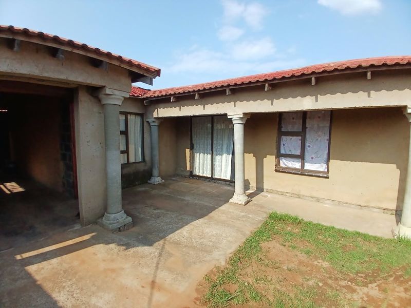 Covered patio area featuring concrete columns and tiled roofing, providing access to the interior through a sliding glass door.