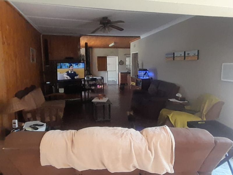 Spacious open-plan living area featuring wood paneling, tiled flooring, a ceiling fan, and a window-mounted air conditioning unit.