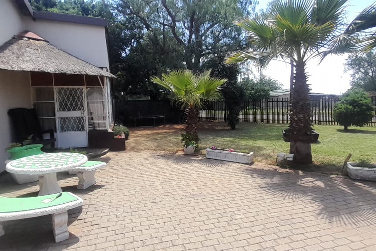 Rear garden featuring a paved patio area with a thatch canopy, established palm trees, and secure perimeter fencing.