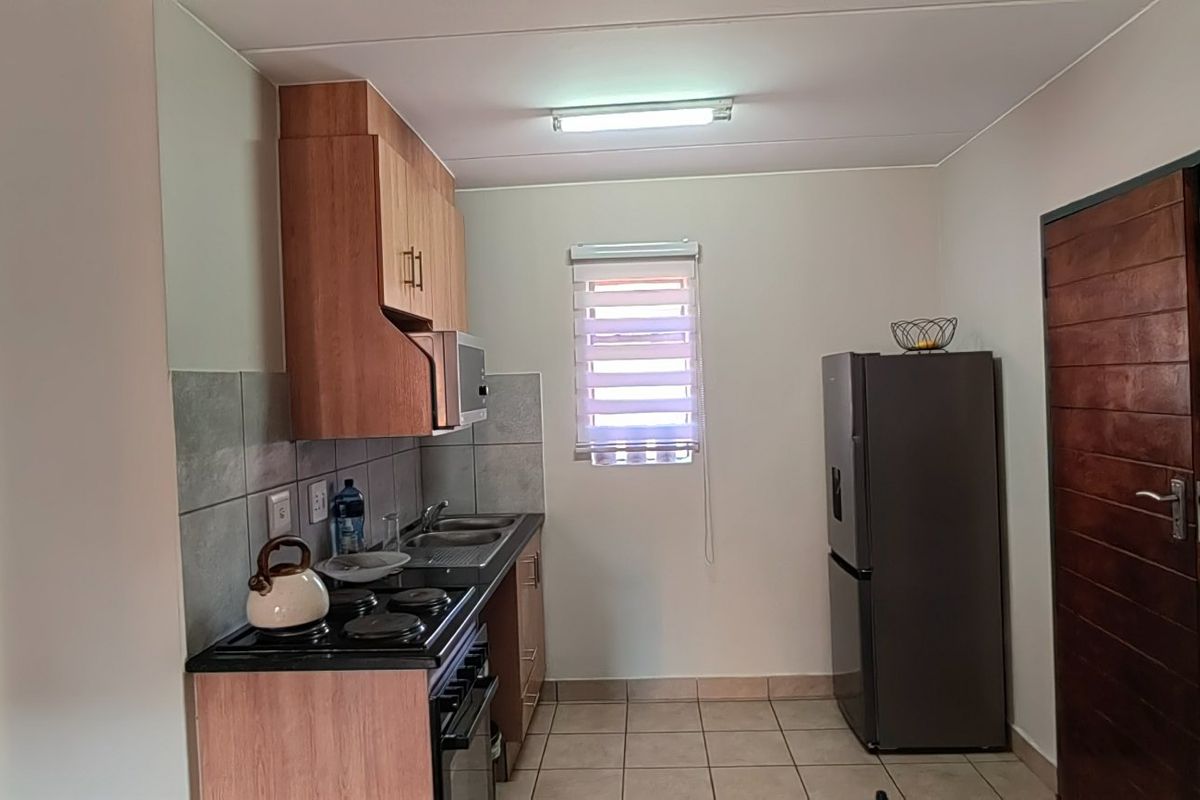 A functional kitchen featuring built-in wooden cabinetry, a stainless steel sink, a built-in stove, and tiled flooring with a neutral backsplash.