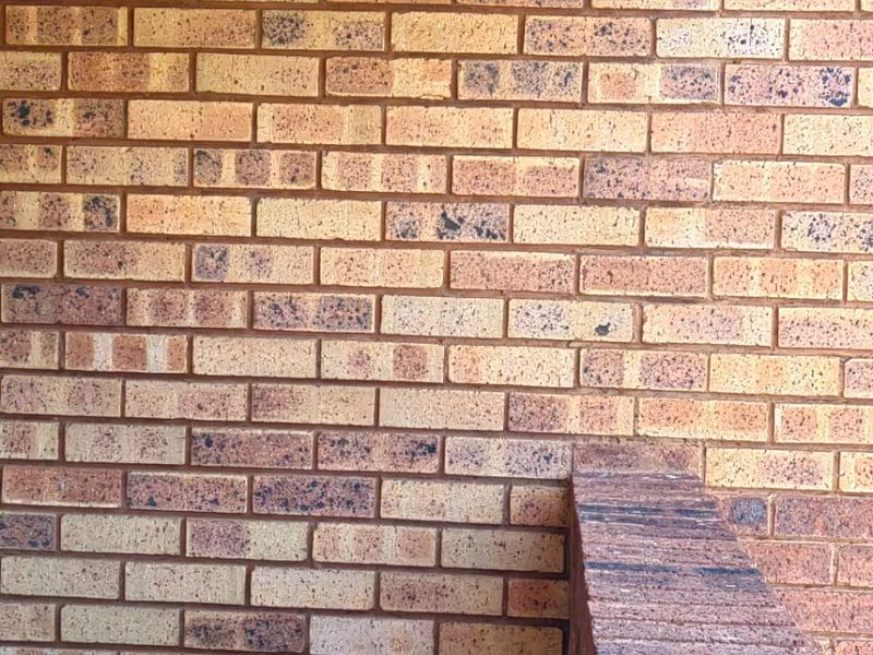 A private balcony area featuring face brick walls, a brick balustrade, and tiled flooring, showing minor signs of water staining on the overhead concrete beam.