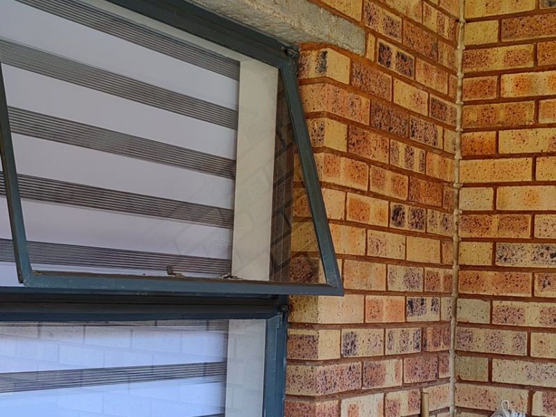A close-up view of a face brick exterior wall featuring a top-hung window with a concrete lintel and brick sill.