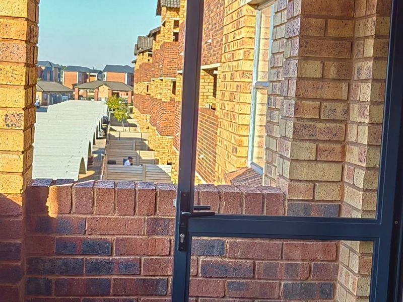 A private balcony featuring durable face brick walls, slate tile flooring, and a secure aluminium framed door overlooking the apartment complex.