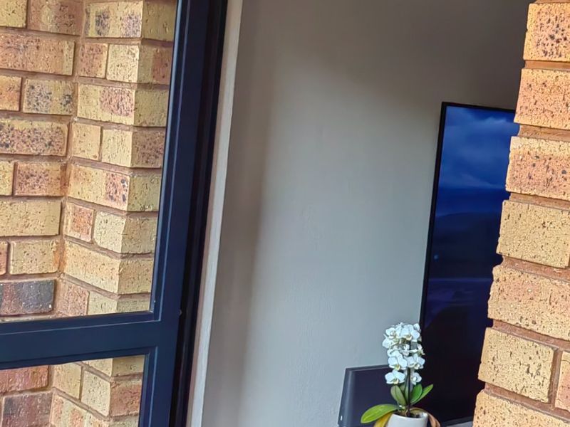 A view from a brick-walled patio looking into an interior living space through an aluminium framed door.