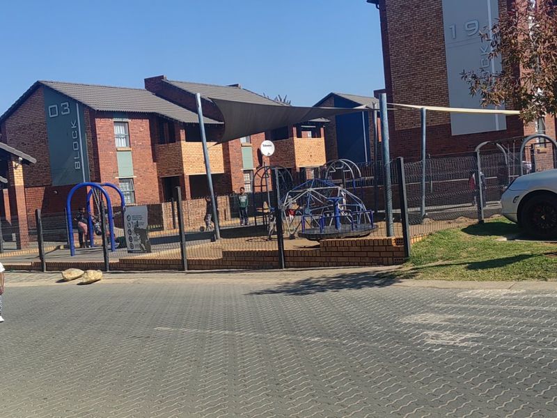 Exterior view of an apartment complex featuring brick buildings, a paved driveway, and a communal playground area with shade structures.