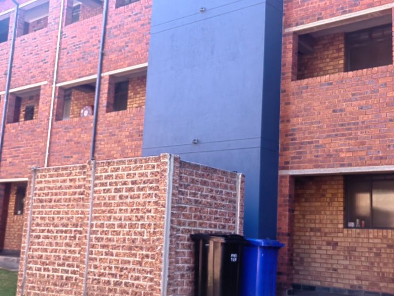 Exterior view of a multi-story apartment building featuring face brick construction with painted blue structural columns and balcony access.