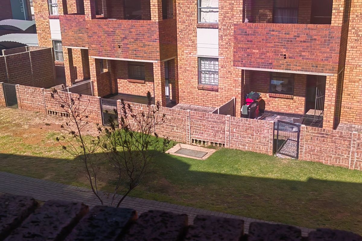 An elevated view of the apartment complex rear exterior, featuring face brick facades, private paved patios, and a shared garden area with paved walkways.